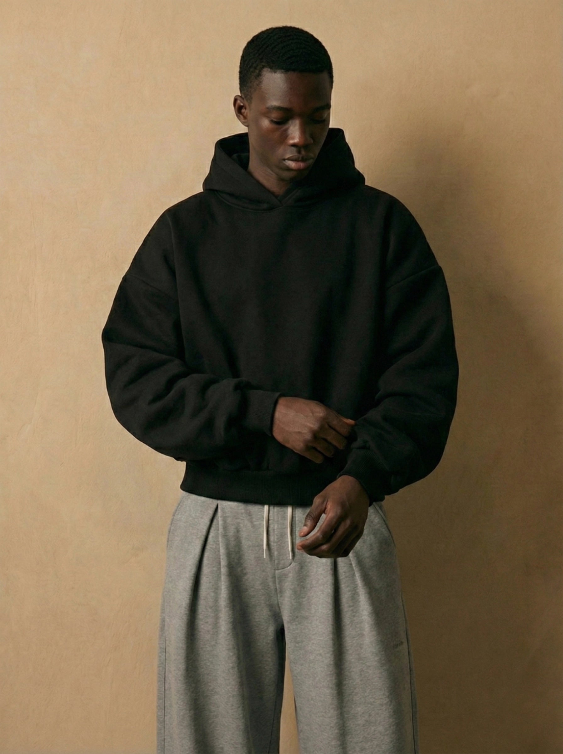 Person wearing a black hoodie and gray pants against a beige background
