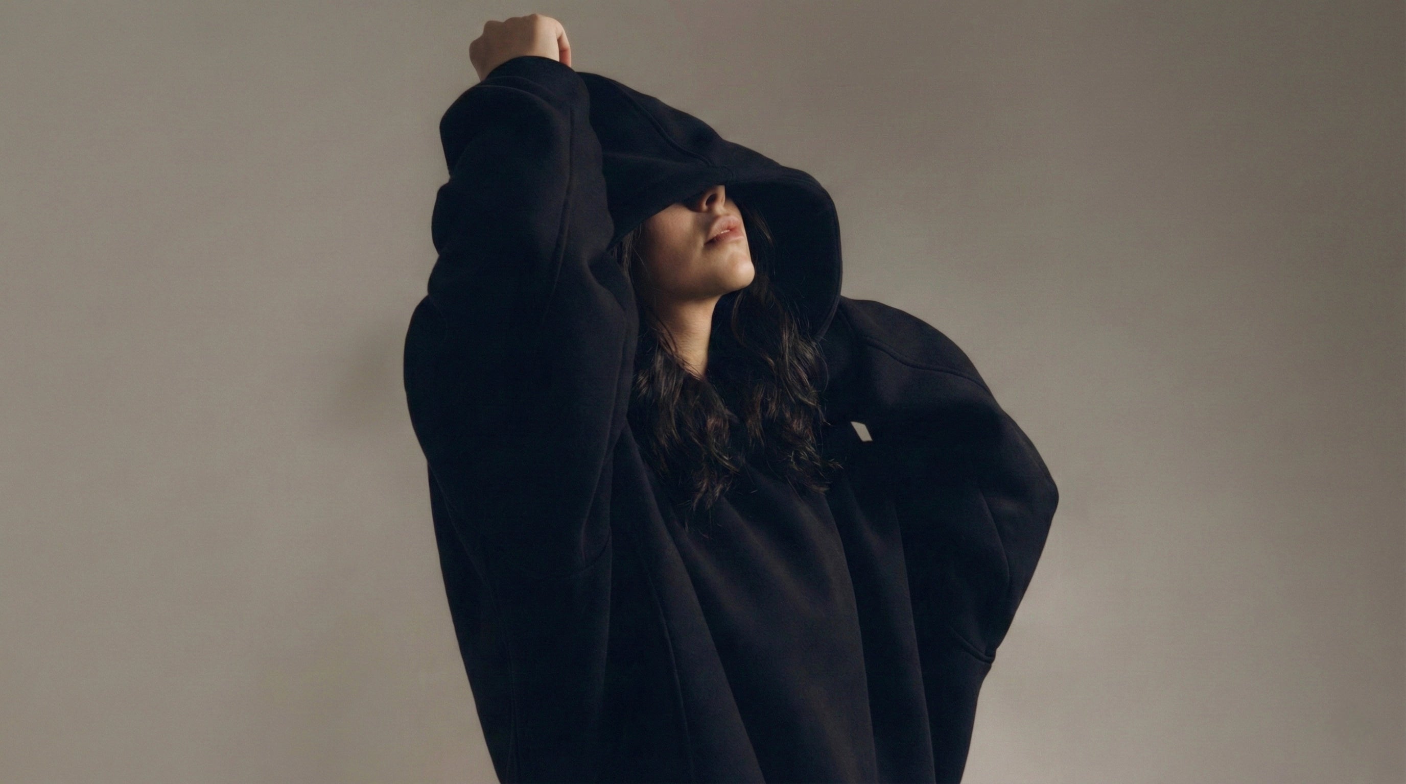 Person wearing a black hooded coat against a plain background