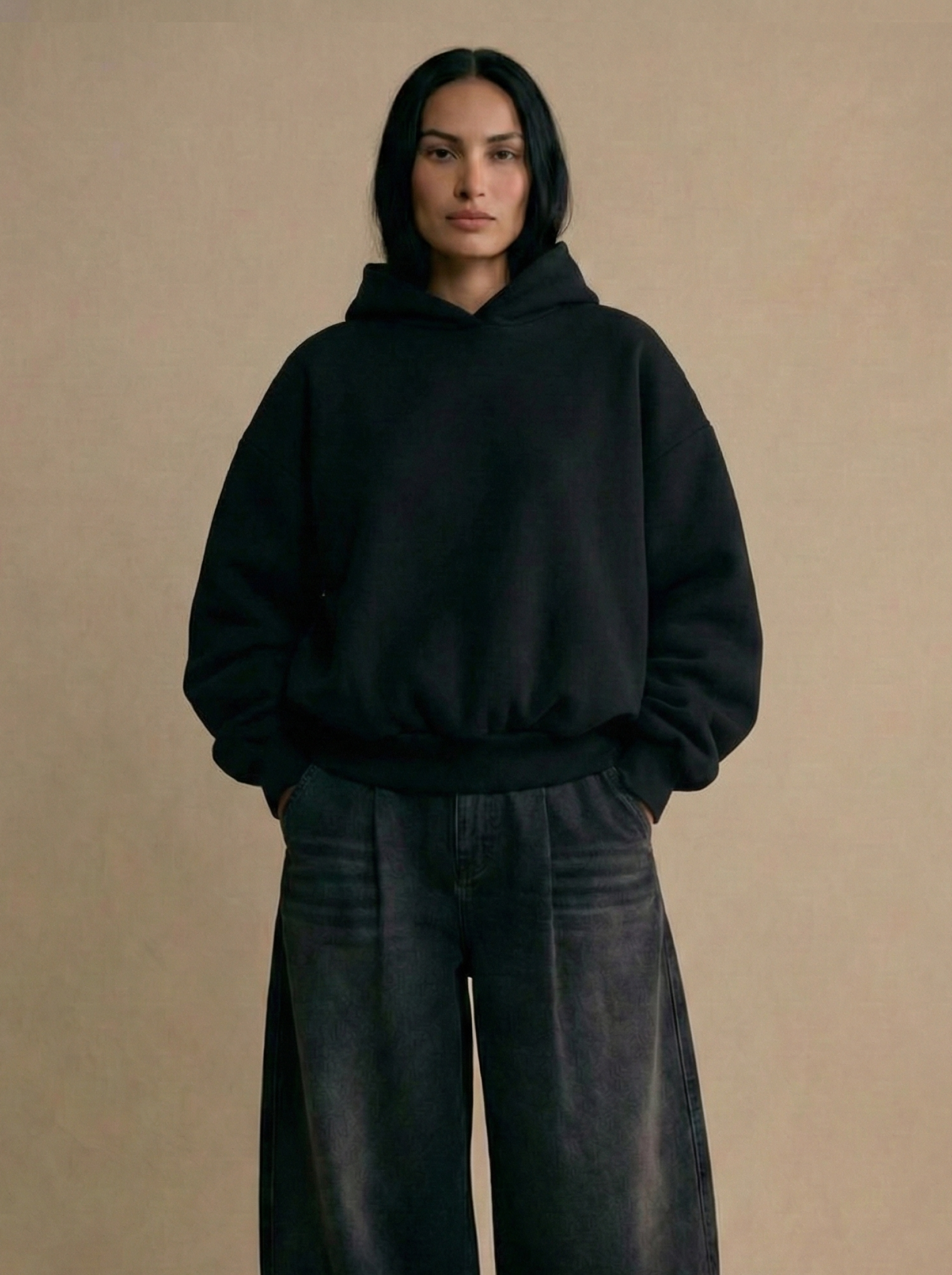 Person wearing a black hoodie and dark pants against a beige background